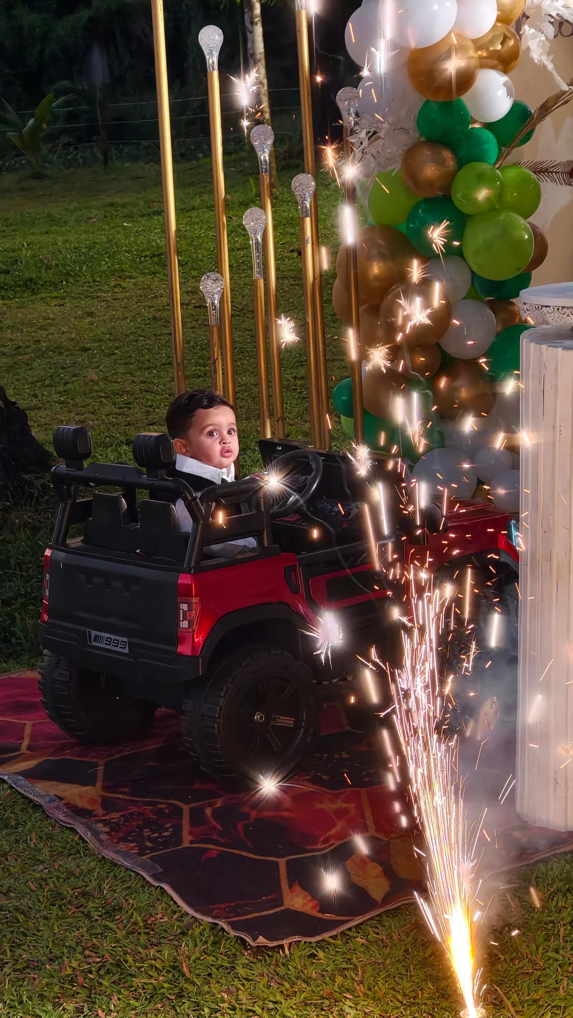 Child in a red toy car beside birthday balloons and sparklers at Terrabithia in Thrissur